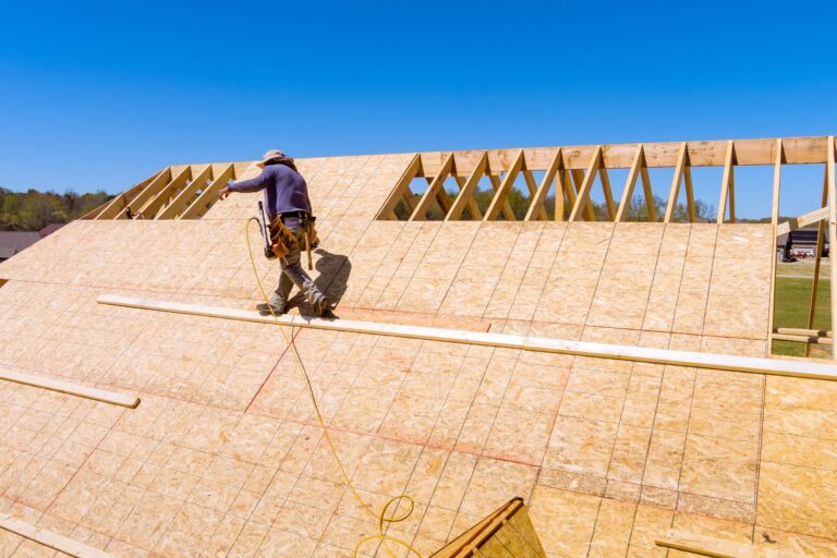 Rooftop construction worker installing plywood panel for roof replacement.